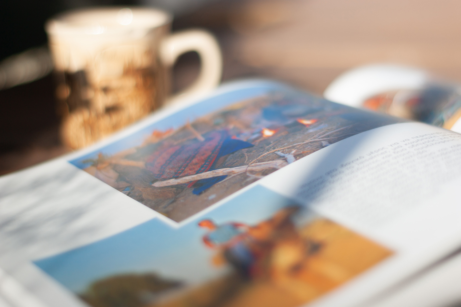 An open book on a table with a coffee mug nearby. The book displays colorful clothing and a picture of a person riding a camel, accompanied by text.